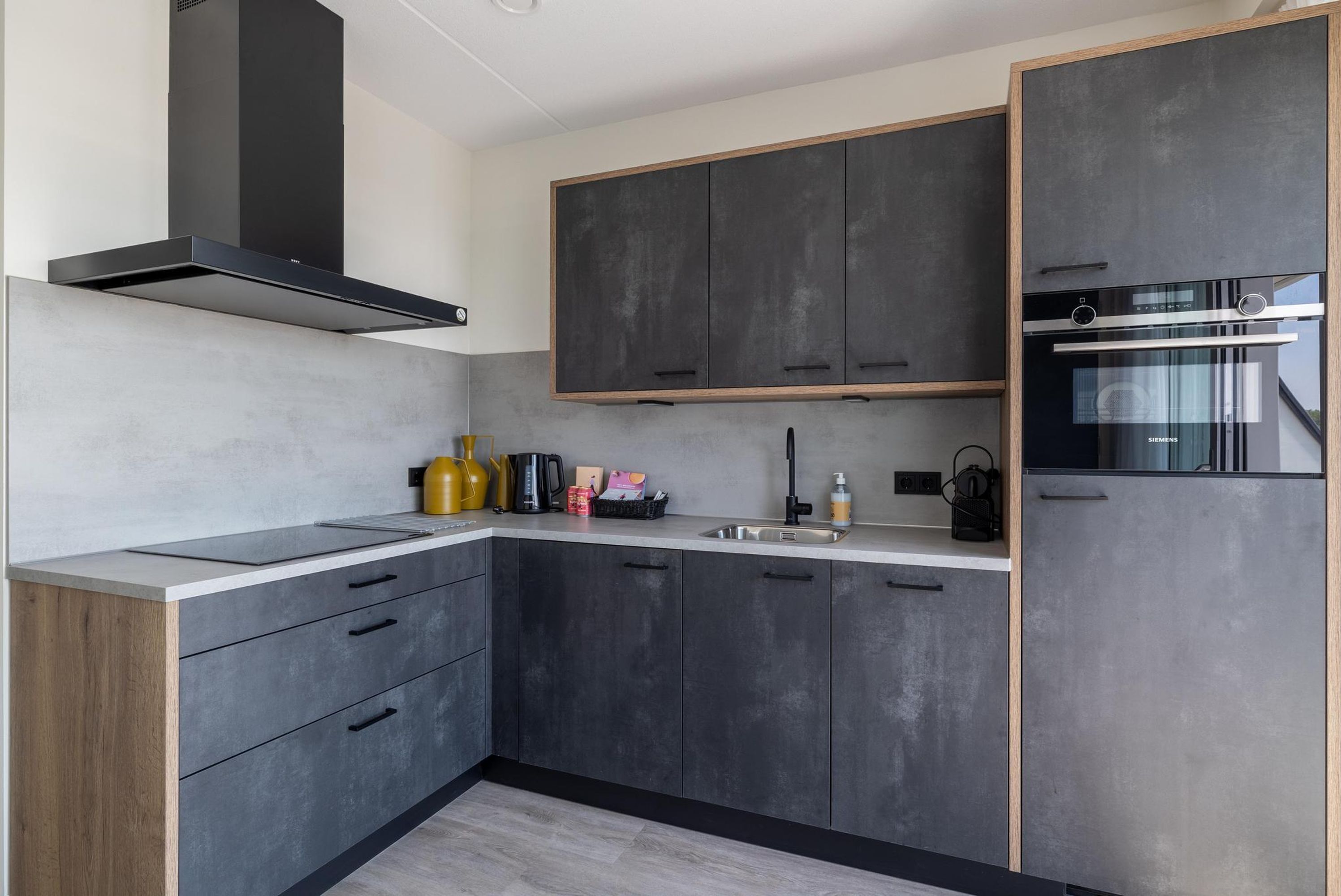 A modern kitchen with grey cabinets, a black range hood, and a built-in oven.