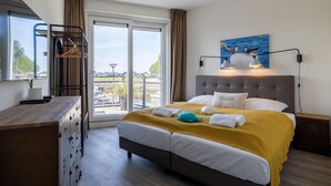 A hotel room with a bed, a desk, a dresser, a window with a view, and a painting on the wall. - Lux Apvm Lagunab-havenw 8-32 S-annaland (Sint-Annaland)