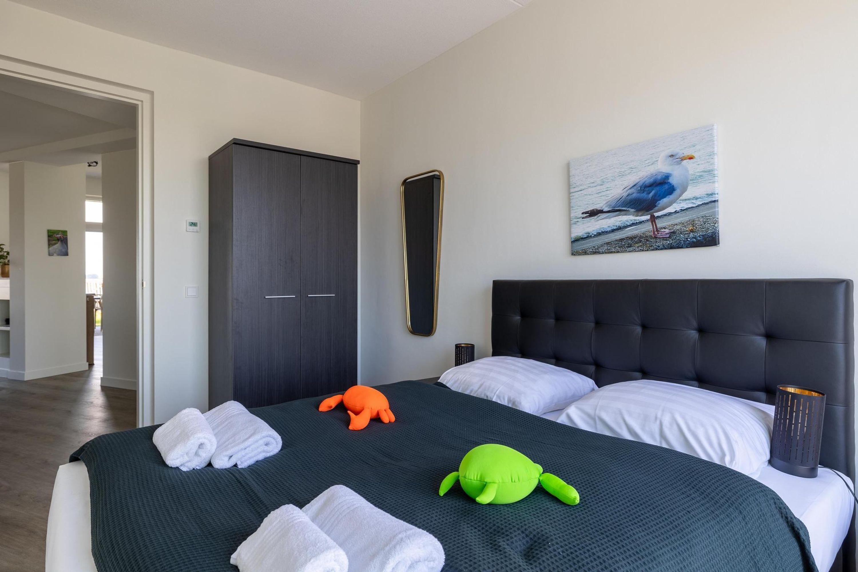 Ein Schlafzimmer mit dunklem Kopfteil, einem großen Spiegel, einem Gemälde einer Möwe und weichen Plüschfiguren auf dem Bett.