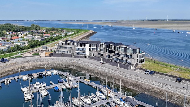 A marina with boats docked, a modern building with balconies, and a clear view of the water and distant shoreline. - Lux Apvm Lagunab-havenw 8-32 S-annaland (Sint-Annaland)