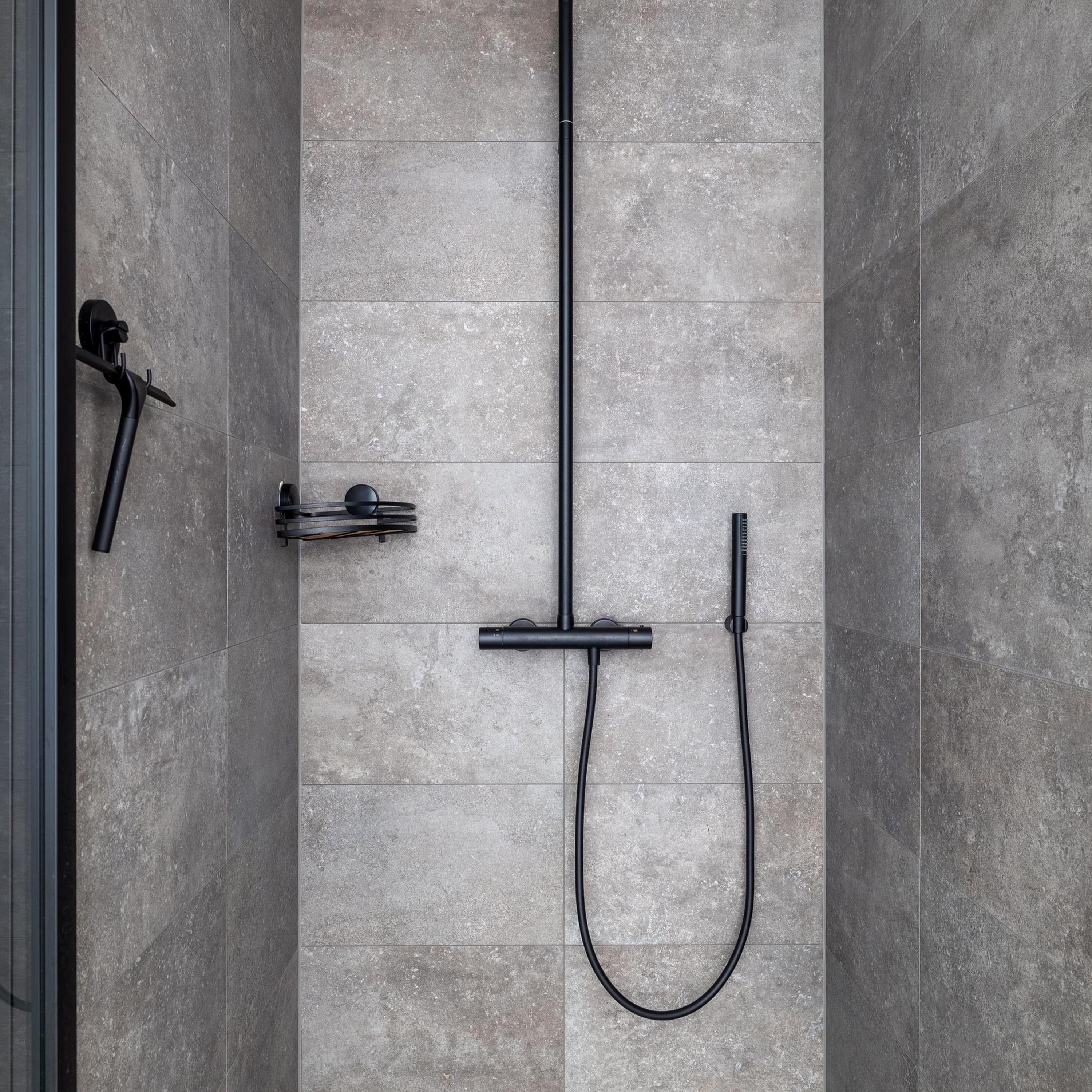 A modern shower with a straight hose and a handheld showerhead, mounted on a tiled wall.