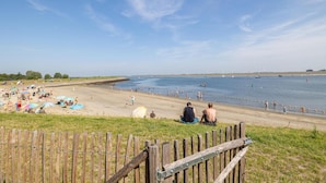 A beach with people sunbathing and swimming, a wooden fence in the foreground, and wind turbines in the distance. - Lux Apvm Lagunab-havenw 8-32 S-annaland (Sint-Annaland)