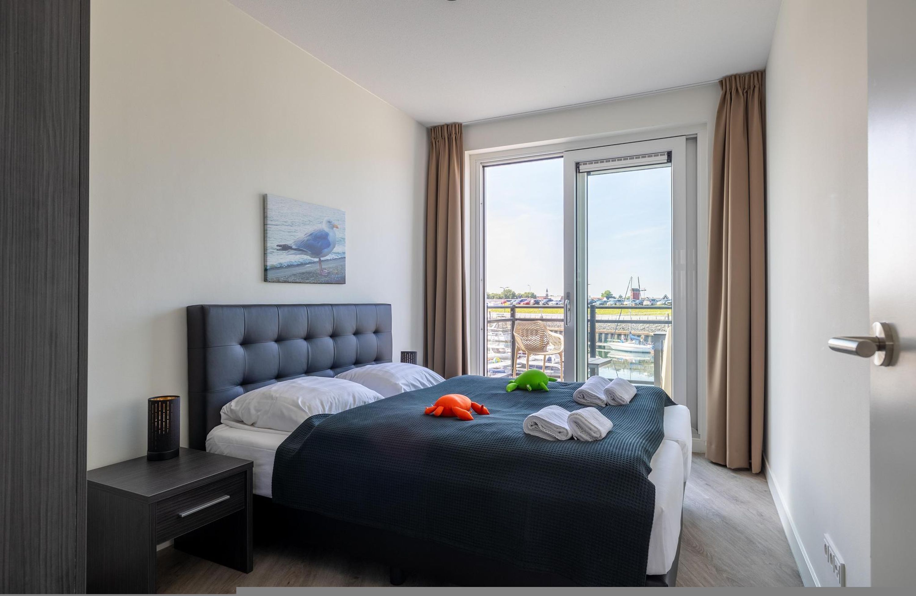 A modern hotel room with a large bed, a nightstand, a painting on the wall, and a view of the city through the window.