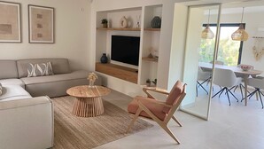 A modern living room with a sofa, a round wooden coffee table, a pink chair, and a TV mounted on a wooden shelf. - Fantastic family villa within walking distance to the beach! (Teulada)
