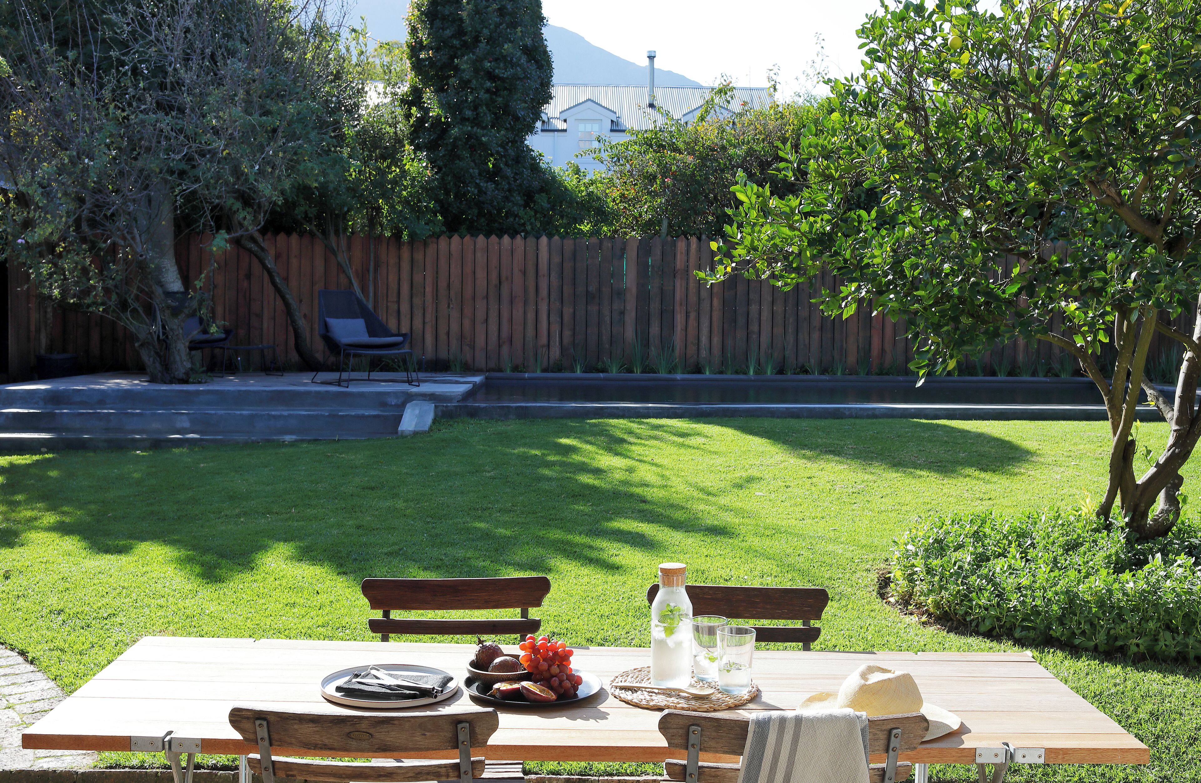 Una mesa de madera al aire libre, con un césped, una valla de madera y un árbol.