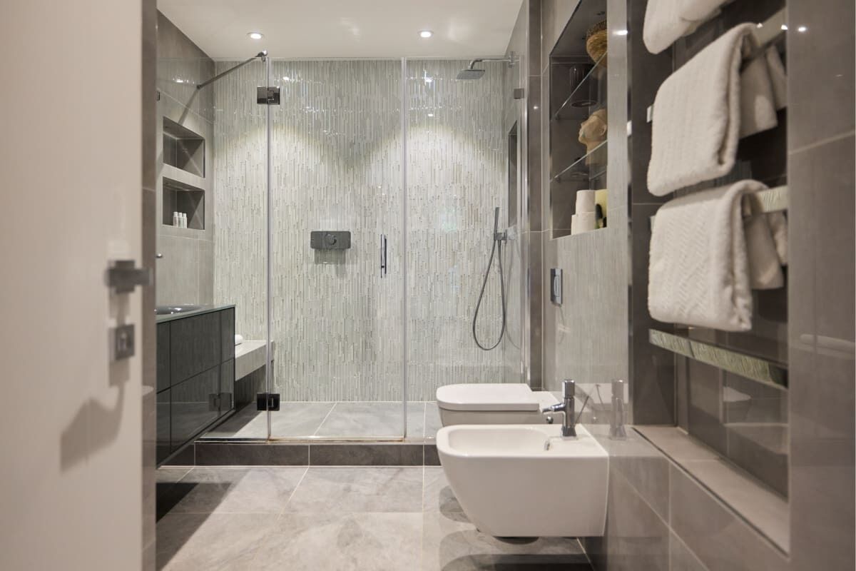 A modern bathroom with a glass-enclosed shower, a white sink, and a towel rack.