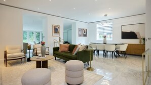 Ein geräumiges Wohnzimmer mit einem grünen Sofa, beigen Sesseln, einem Couchtisch und einem Essbereich mit Tisch und Stühlen.