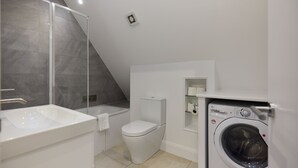 Casa de banho moderna com chuveiro, sanita, lavatório e máquina de lavar roupa.