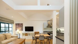 Um espaço moderno para relaxar, com sofá, mesa de centro, mesa de jantar e cadeiras. Possui área de cozinha com eletrodomésticos e uma TV de tela plana na parede.