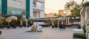A courtyard with outdoor seating, white tables, and chairs, surrounded by greenery and white flowers. - ARC The Boutique Hotel (Bhubaneshwar)