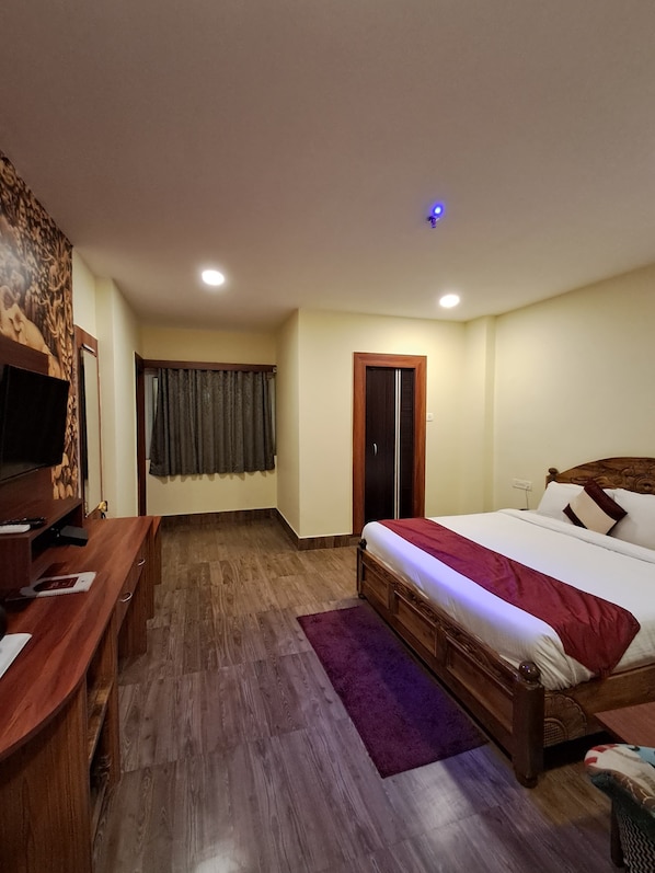 A bedroom with a wooden bed, a desk with a chair, a television, and a door. - ARC The Boutique Hotel (Bhubaneshwar)