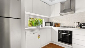 Een moderne keuken met witte kastjes, een ingebouwde vaatwasser, een magnetron, een fornuis en een raam met uitzicht op groen.
