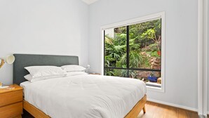 Een slaapkamer met een groot raam, een bed, een nachtkastje en een lamp.