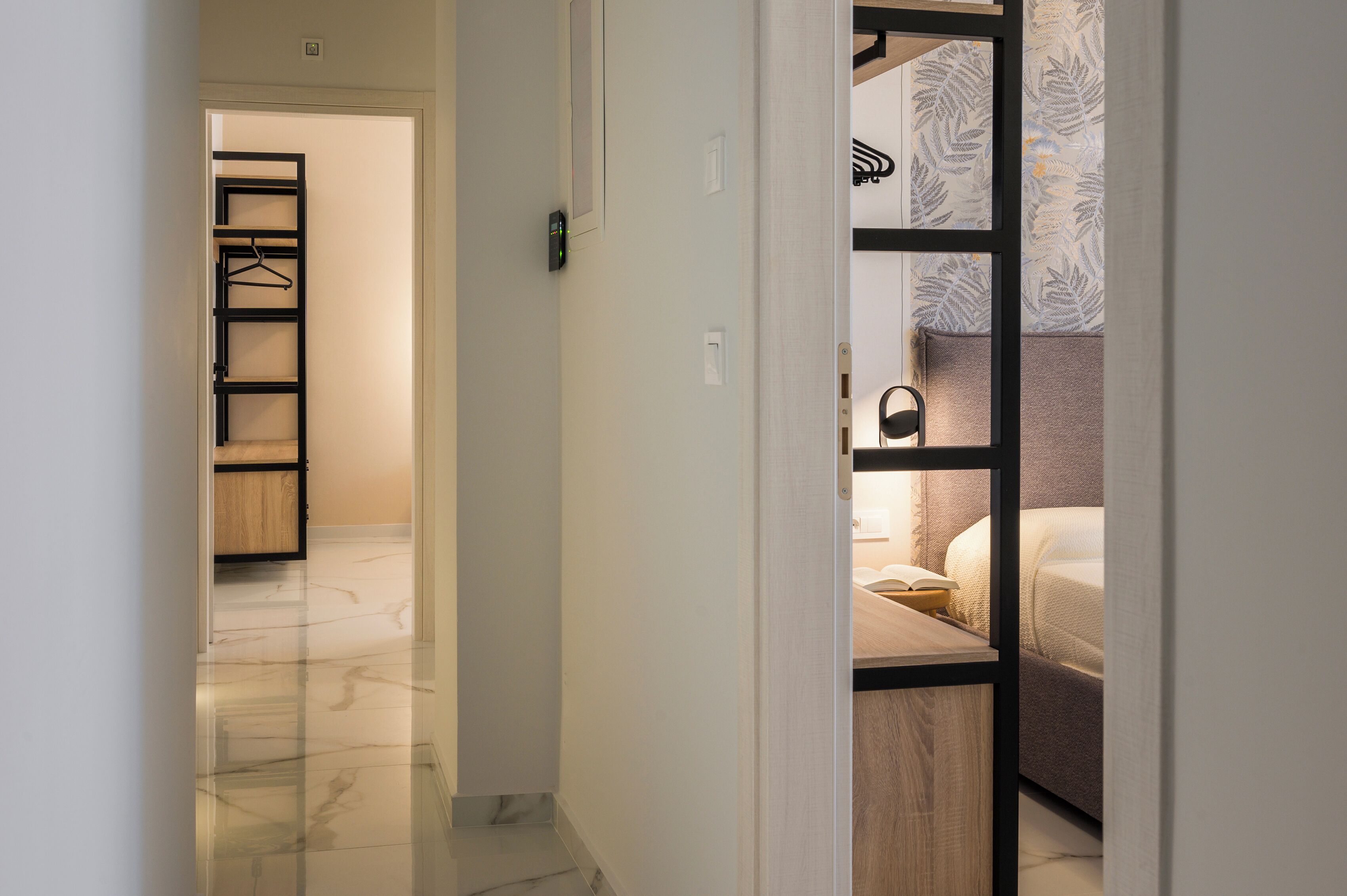Un pasillo que conduce a un dormitorio con cama, mesita de noche y lámpara colgante.