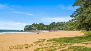 Una spiaggia con vista libera sull'oceano, una zona verdeggiante e edifici sullo sfondo.