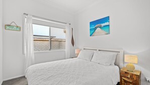 Camera da letto con un letto grande, una finestra con tende, un cartello a tema spiaggia e un dipinto raffigurante una spiaggia.