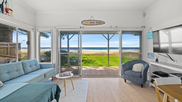 Un soggiorno moderno con un'ampia porta-finestra scorrevole che si apre su un balcone con vista sulla spiaggia.