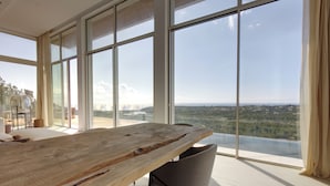 A spacious room with a large wooden table and a view of a cityscape through large windows. - Villa Tigliola (Zonza)