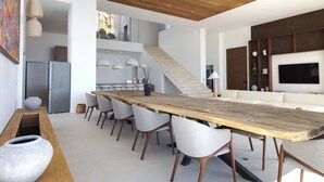 A modern kitchen with a long wooden table, white chairs, and a staircase leading to an upper level. - Villa Tigliola (Zonza)