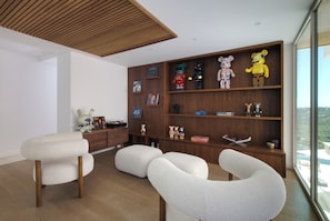 A modern living room with a wooden ceiling, white upholstered chairs, and a wooden bookshelf filled with toys and figurines. - Villa Tigliola (Zonza)