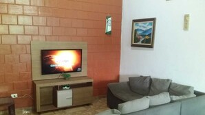 A living room with a TV on a wooden stand, a grey sofa, and a brick wall. - Beautiful farm in Jarinu (Caioçara Jarinu)