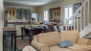 Een ruime woonkamer met een beige bank, een eethoek met een houten tafel, en een keuken met groene kastjes.