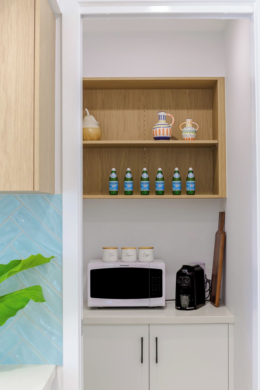 A kitchen with a microwave, a coffee maker, and a shelf with decorative items and bottles.