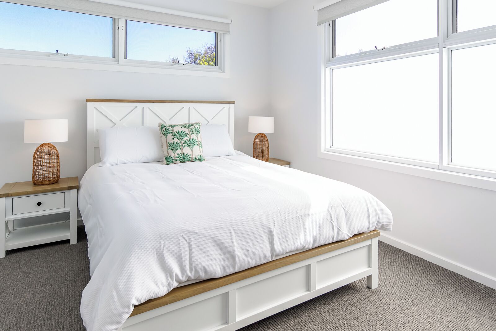 A bedroom with a large bed, white bedding, two bedside tables with lamps, and a view of the sky through a window.