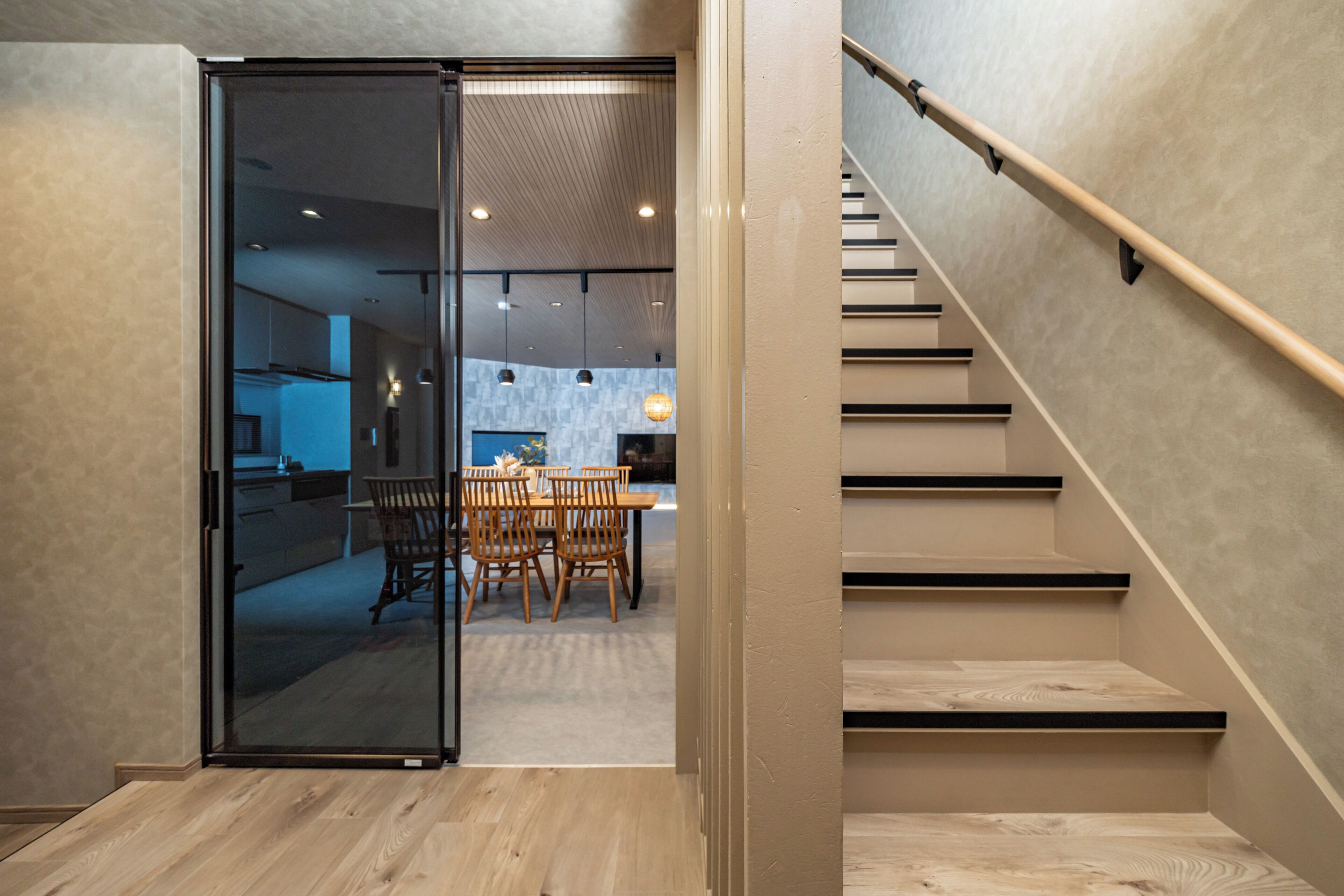 A modern interior with a staircase, wooden flooring, and a dining area with chairs and a table.