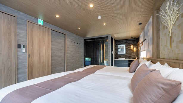A modern hotel room with a large bed, wooden panel walls, a built-in desk, and a bathroom visible through an open door. - JAPAVISTA Yamato (Osaka)
