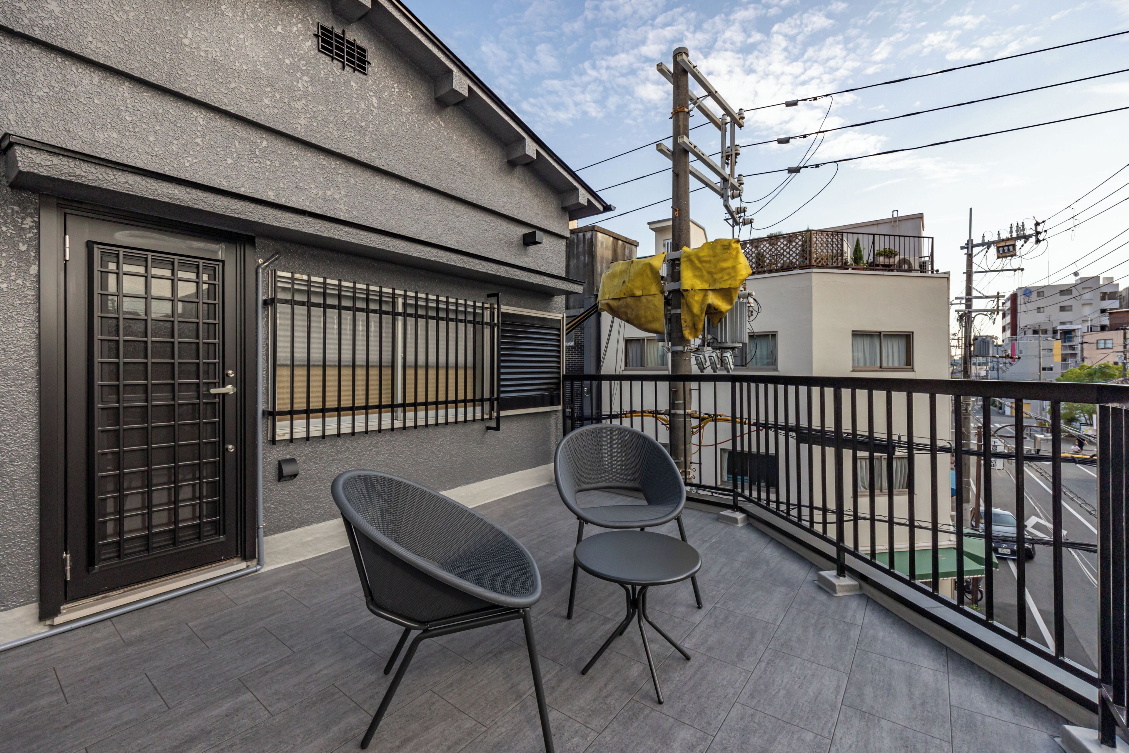 A balcony with two chairs, a covered area with yellow fabric, and a view of the street and buildings.