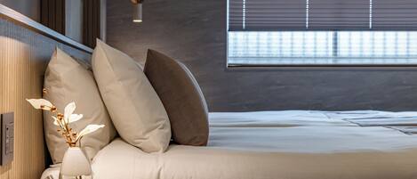 Un dormitorio moderno con cama, almohadas, un jarrón con flores y una mesa redonda.