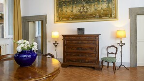 Un comedor con una mesa de madera, un jarrón azul con flores, un armario de madera y dos lámparas de pie.
