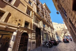 A historic building with a barber shop on the ground floor, parked scooters, and cars on a cobblestone street. - Cartari Deluxe Apartment (Rome)