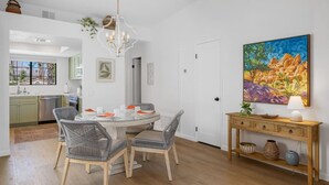 A dining area with a round table, wicker chairs, a chandelier, and a painting on the wall. - Casa Compadre - 2 Bedroom Luxury Condo (Palm Springs)