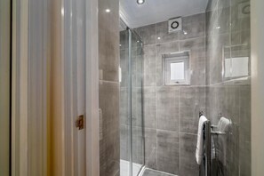 A modern bathroom with a glass shower enclosure, a towel rack, and a small window. - Camden Apartments (London)