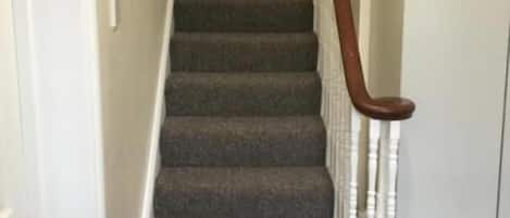 Una escalera alfombrada con barandillas de madera y paredes blancas.