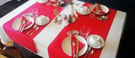 A dining table set with white plates, silverware, and red napkins, surrounded by a red table runner.