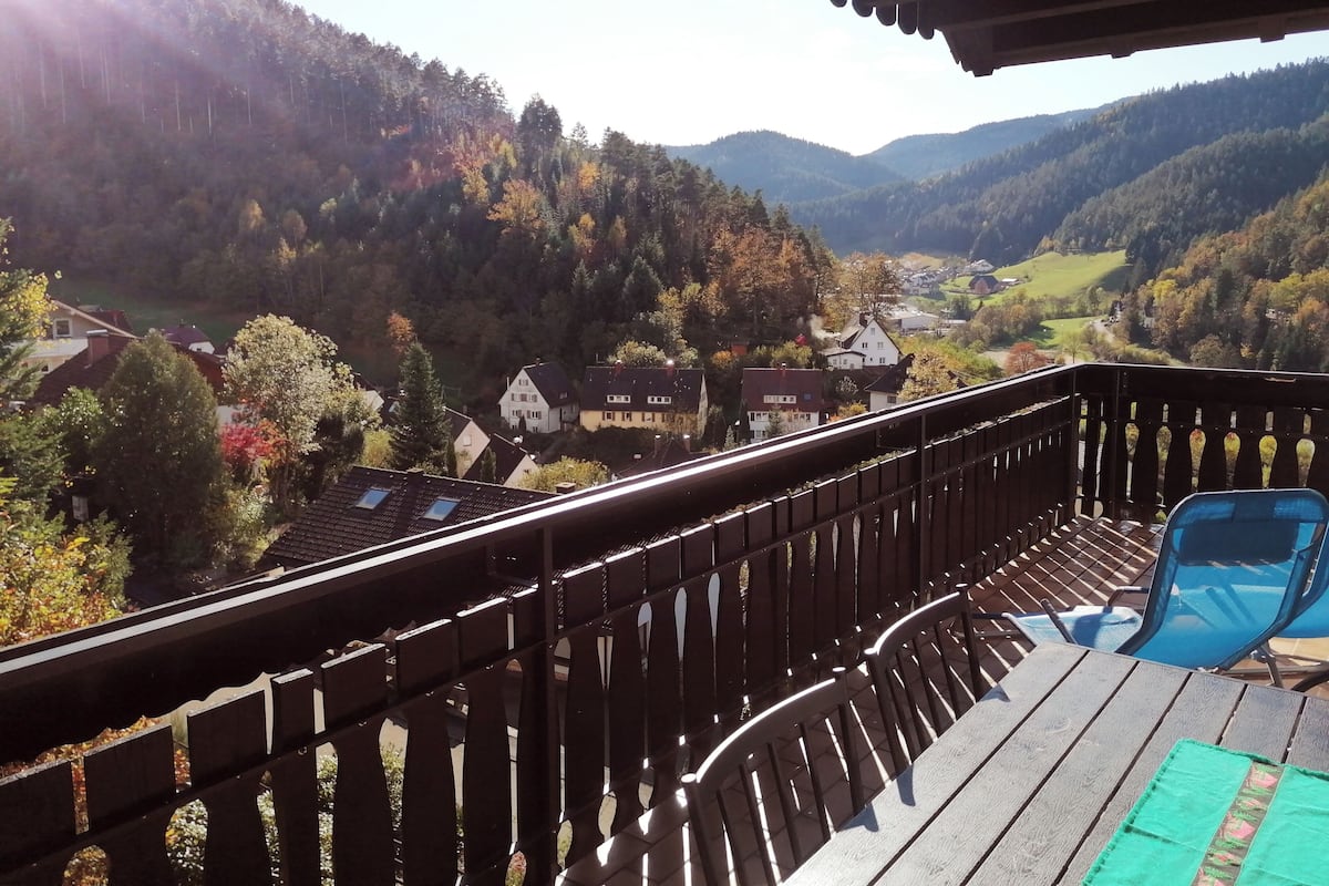 A balcony with a view of a valley, houses, and trees.