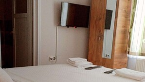 Un dormitorio con cama, televisor montado en la pared y ventana con cortinas.