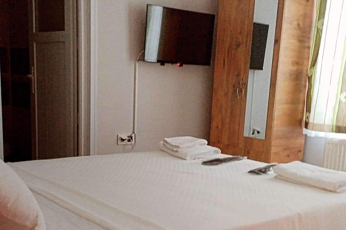 A bedroom with a bed, a TV mounted on the wall, and a window with curtains.