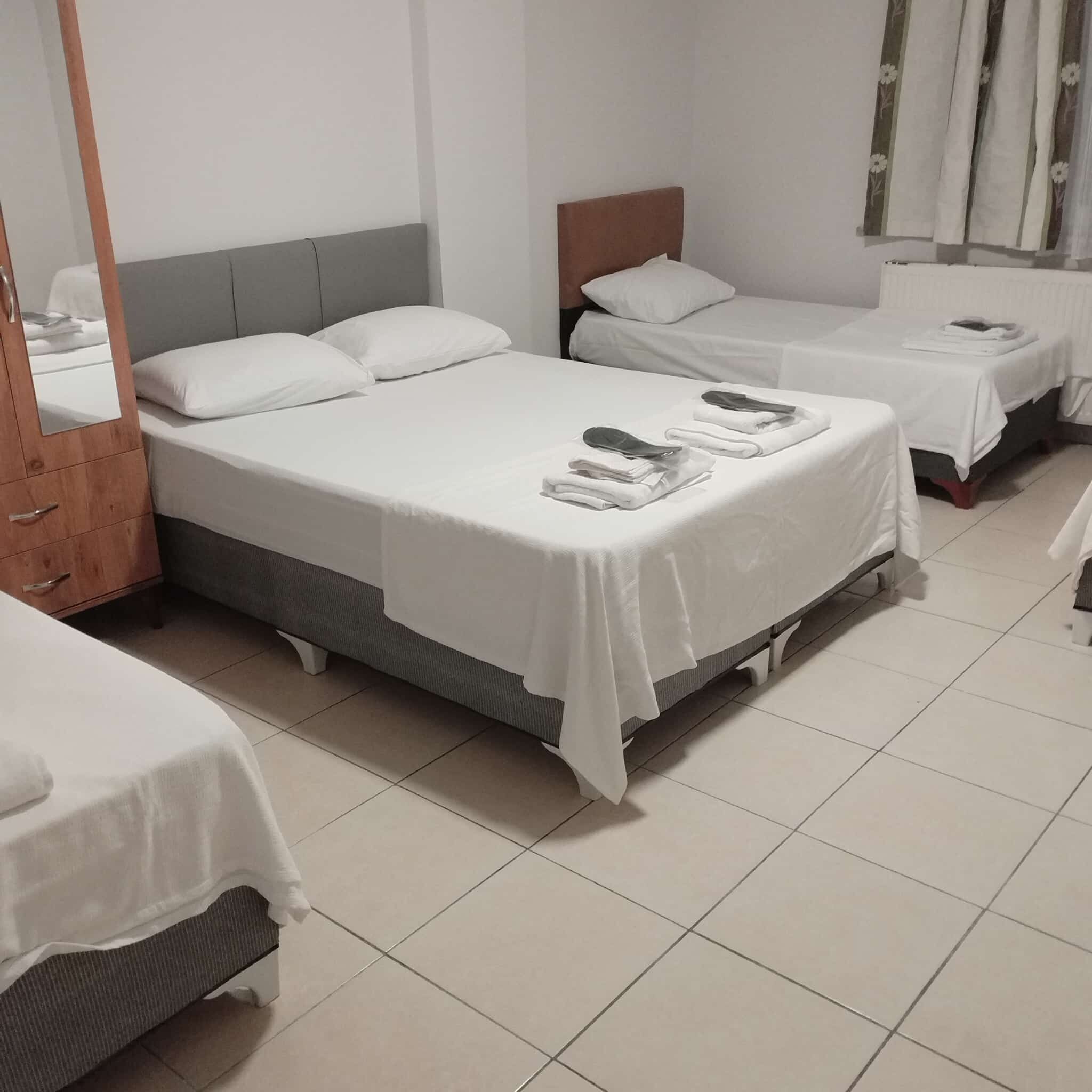 A hotel room with two single beds, a wooden wardrobe, and a small table with a lamp.