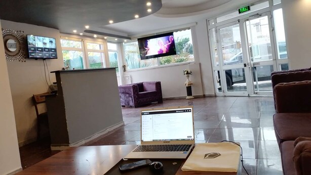 Una zona de recepción con un ordenador portátil sobre una mesa, un televisor en la pared y un sofá al fondo.