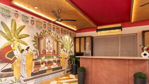 Een hotel lobby met een vloer met geometrisch patroon, een muurschildering van traditionele figuren en een receptiebalie met een bord.