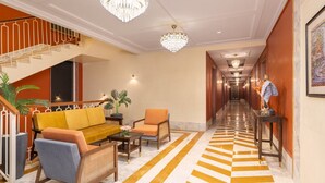 Een hotellobby met een zwart-wit schaakbordvloer, een trap en een receptiebalie.