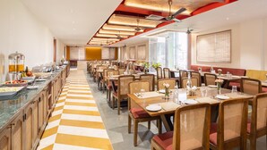 Een ruime eetruimte met lange tafels en stoelen, een geruit vloertje en een buffet aan één kant.