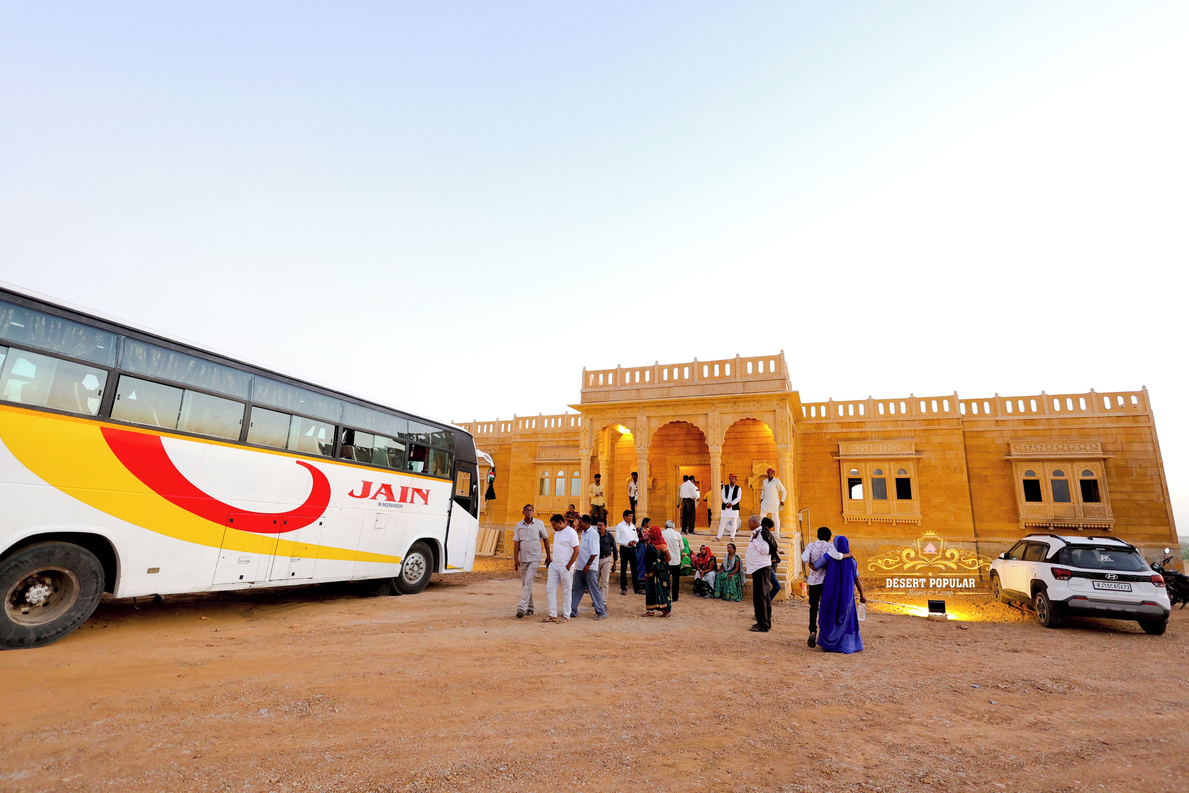A group of people standing in front of a building with a large bus parked nearby.
