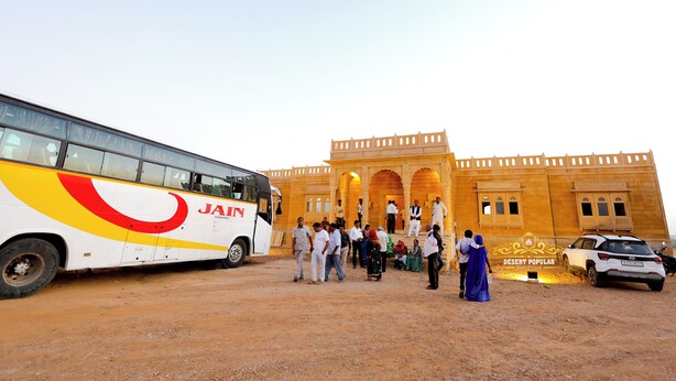 A group of people standing in front of a building with a large bus parked nearby. - Desert Popular Resort & Camp (Jaisalmer)