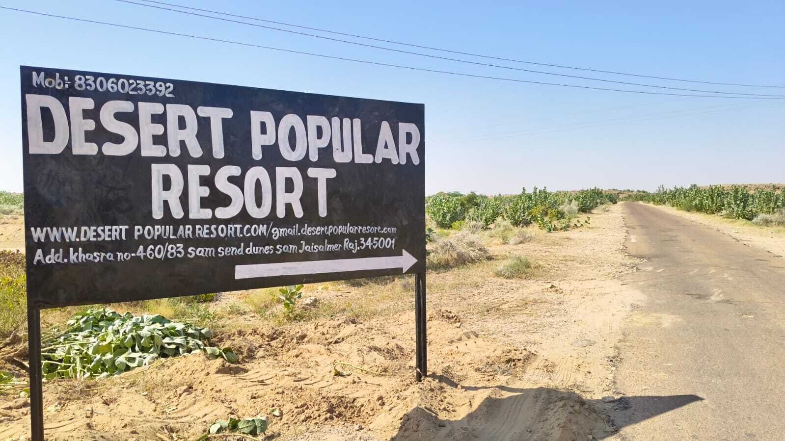 A sign for Desert Popular Resort with contact information and directions.