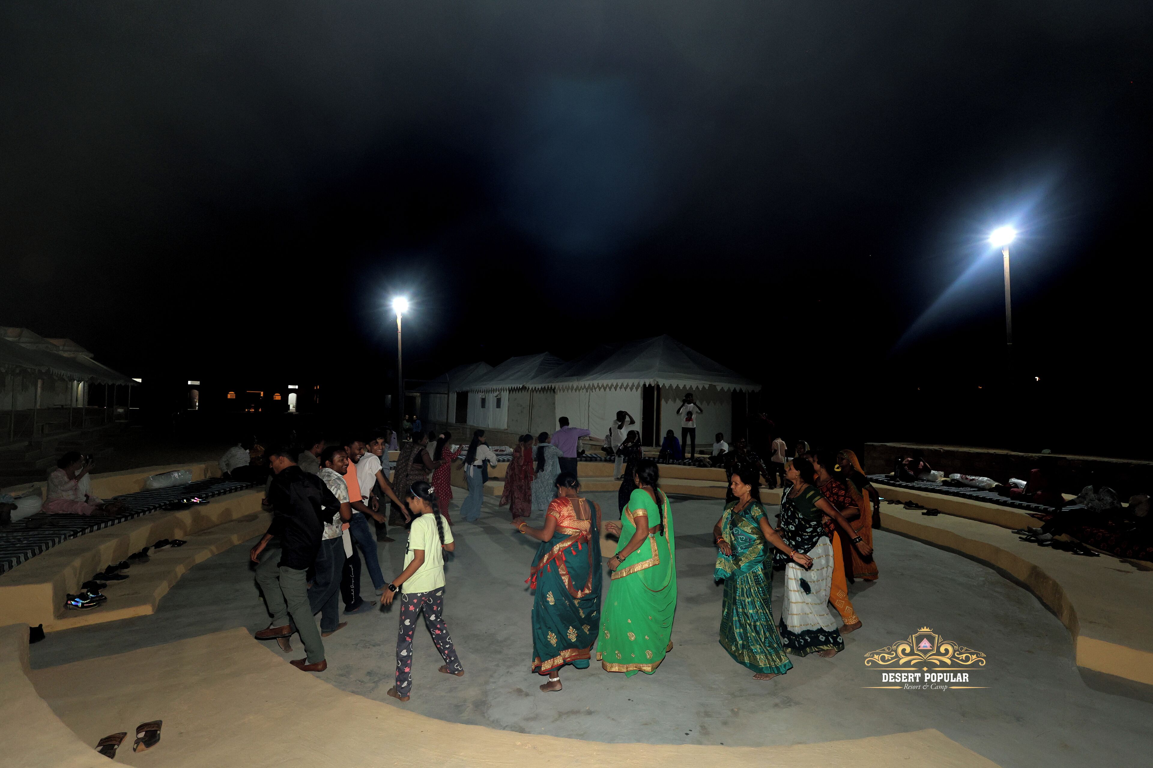 A group of people gathered around a stage with a tent in the background, under night-time lighting.